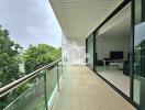 Spacious balcony with glass railing and view of surrounding greenery, adjacent to a modern living room.