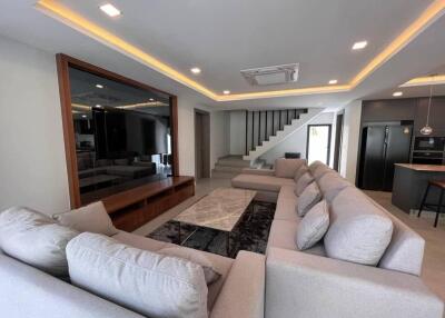 Modern living room with large sectional sofa, marble coffee table, recessed lighting, and staircase.