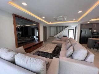 Modern living room with large sectional sofa, marble coffee table, recessed lighting, and staircase.