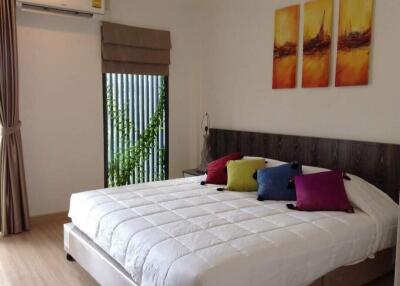 Cozy bedroom with bed, pillows, artwork, and window with potted plant.