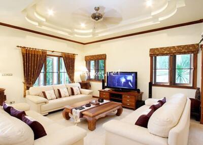 Well-furnished living room with cream sofas, wooden furniture, and a TV