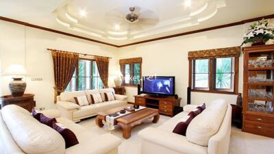 Well-furnished living room with cream sofas, wooden furniture, and a TV