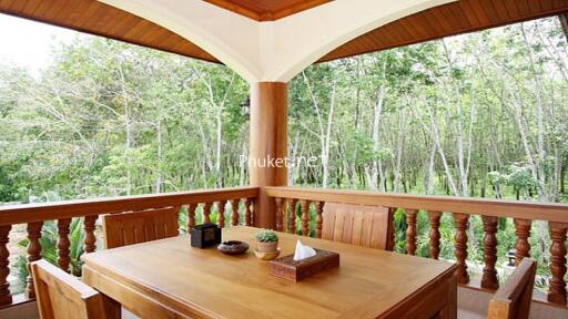 Wood-furnished balcony with outdoor dining table set overlooking greenery