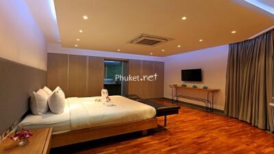 Spacious, modern bedroom with wooden flooring, a large bed, and a flat-screen TV.