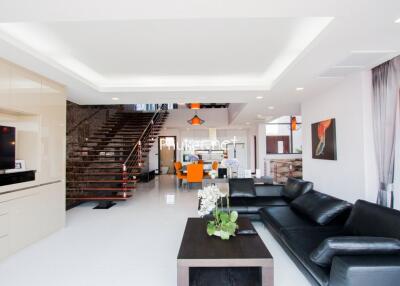 Modern living room with black leather sofa, coffee table, flat-screen TV, and open-plan dining area with stairs.