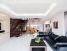 Modern living room with black leather sofa, coffee table, flat-screen TV, and open-plan dining area with stairs.