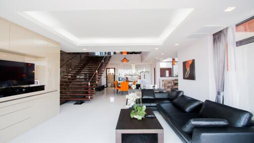 Modern living room with black leather sofa, coffee table, flat-screen TV, and open-plan dining area with stairs.