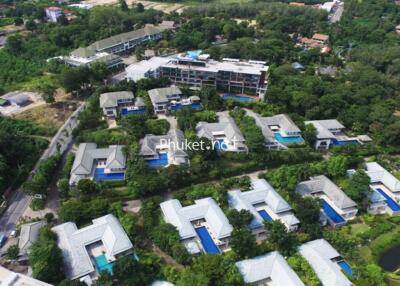 Aerial view of residential community with multiple houses and pools in a lush green area