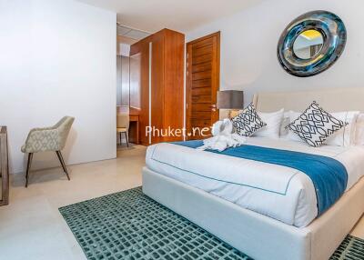 Cozy and modern bedroom with a neatly made bed, cushioned chair, mirror, and wooden elements