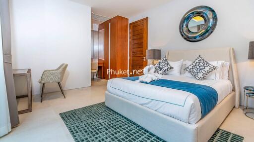 Cozy and modern bedroom with a neatly made bed, cushioned chair, mirror, and wooden elements