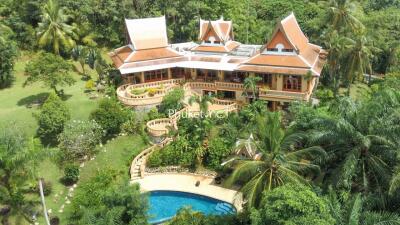 Large Thai-style villa with red roofs, surrounded by lush greenery and a swimming pool