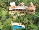 Large Thai-style villa with red roofs, surrounded by lush greenery and a swimming pool