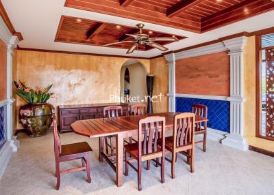 Interior view of a dining room with wooden table and chairs, decorative ceiling, and large vase with plants.