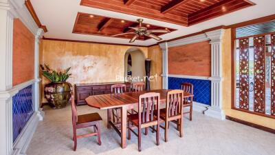 Interior view of a dining room with wooden table and chairs, decorative ceiling, and large vase with plants.