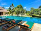 Outdoor pool area with lounge chairs and surrounded by tropical greenery