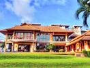 Front view of a luxurious, tropical-style house with manicured lawn and palm trees