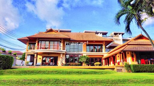 Front view of a luxurious, tropical-style house with manicured lawn and palm trees