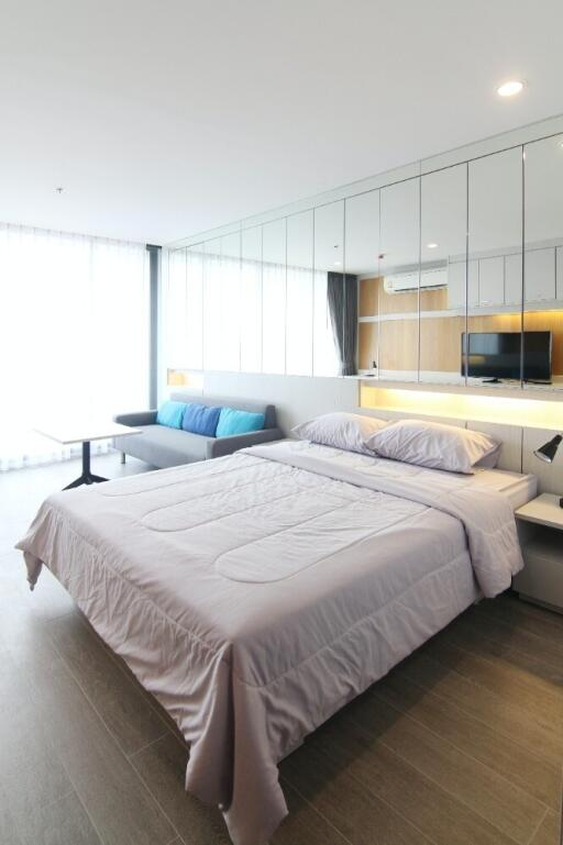 A modern bedroom with a large bed, sofa, and mirrored wall