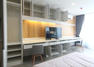Modern bedroom with open wardrobe cabinets, a wall-mounted TV, and a study area