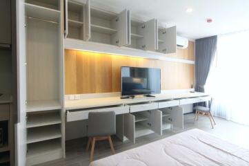 Modern bedroom with open wardrobe cabinets, a wall-mounted TV, and a study area