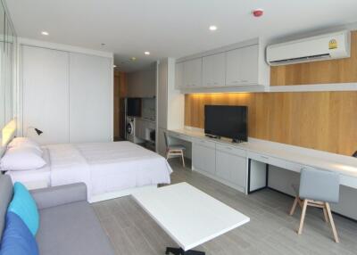 Modern studio apartment bedroom with a bed, sofa, large TV, desk, and air conditioning unit.