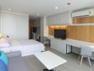 Modern studio apartment bedroom with a bed, sofa, large TV, desk, and air conditioning unit.