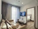 A modern living room with a beige sofa, a wall-mounted TV, and a view into the bedroom