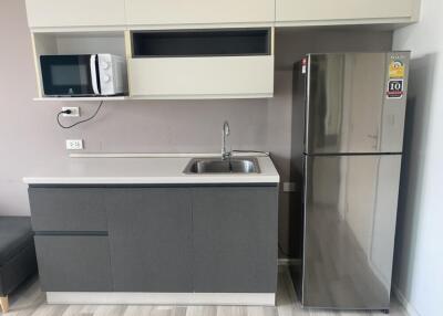 Modern kitchen with gray cabinets, stainless steel fridge, microwave, sink, and white countertops