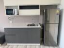 Modern kitchen with gray cabinets, stainless steel fridge, microwave, sink, and white countertops