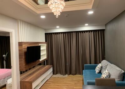 Modern living room with wooden floor, brown curtains, blue sofa, mounted TV, and chandelier