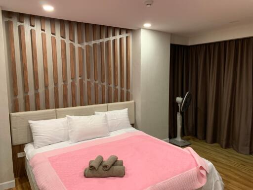 Master bedroom with modern wooden wall design, double bed and floor fan