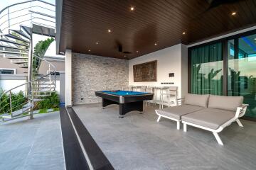 Modern outdoor living area with a pool table, seating, and spiral staircase