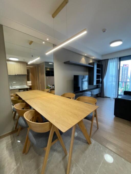 Modern living and dining area with large wooden table, TV, and large window