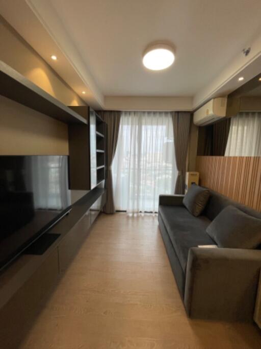 Modern living room with large window, grey sofa, and built-in shelving