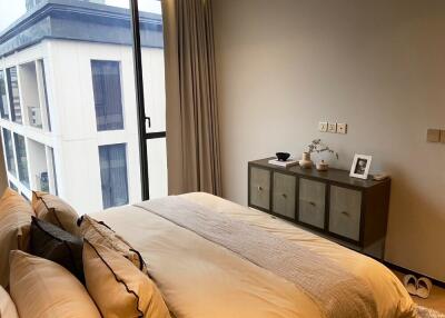 Modern bedroom with a large window and a view, featuring a bed with decorative pillows and a cabinet with decor items