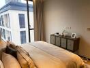 Modern bedroom with a large window and a view, featuring a bed with decorative pillows and a cabinet with decor items