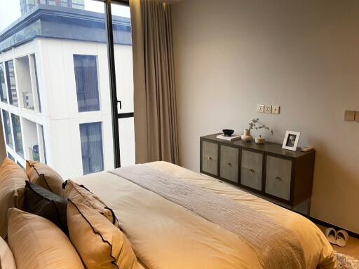 Modern bedroom with a large window and a view, featuring a bed with decorative pillows and a cabinet with decor items