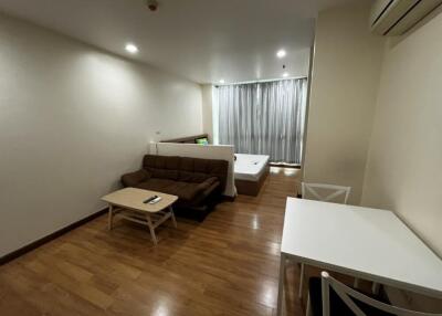 Modern studio apartment with a wooden floor, small sofa, coffee table, bed, and dining table with chairs