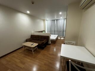 Modern studio apartment with a wooden floor, small sofa, coffee table, bed, and dining table with chairs