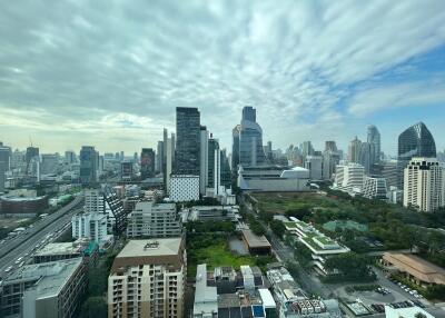 View of city skyline with tall buildings, greenery, and cloudy sky