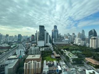 View of city skyline with tall buildings, greenery, and cloudy sky