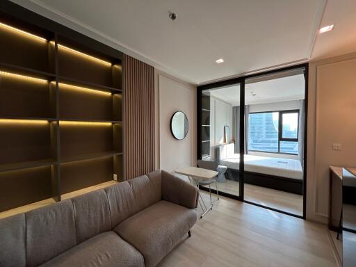 Modern living room with sofa, shelves, and a view into the bedroom