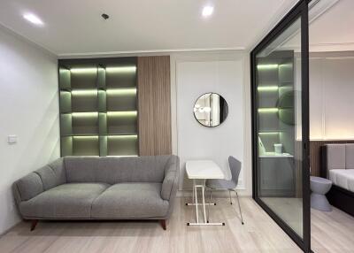 Modern living room with an upholstered sofa, stylish shelving unit, glass partition, and a small dining area.