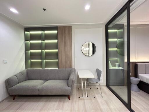 Modern living room with an upholstered sofa, stylish shelving unit, glass partition, and a small dining area.