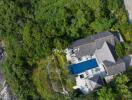 Aerial view of a house with a pool surrounded by lush greenery and located near the coast