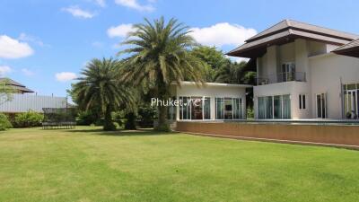 Exterior view of a large house with a spacious lawn and palm trees