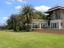 Exterior view of a large house with a spacious lawn and palm trees