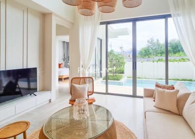 Bright and airy living room with large glass doors, modern furnishings, and view of a garden and pool.