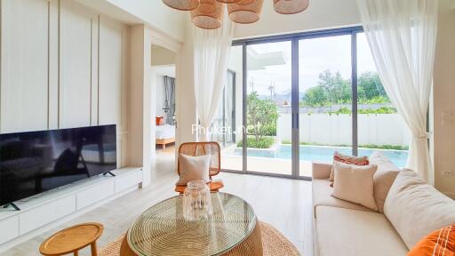 Bright and airy living room with large glass doors, modern furnishings, and view of a garden and pool.