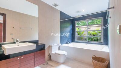 Modern bathroom with large window, bathtub, toilet, sink and wooden cabinetry